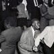 A black and white photo of two men and a woman dancing, on a crowded dance floor