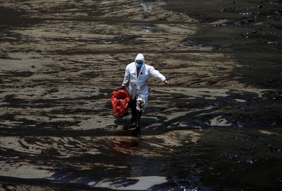 A worker carries oil-fouled material across a polluted beach.