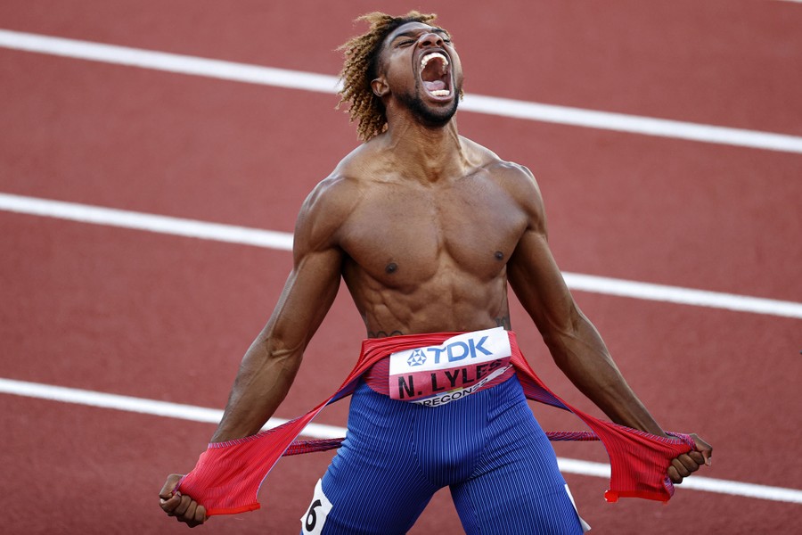 An athlete tears off his shirt and shouts in celebration on a running track.