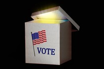 A white ballot box with the American flag above the word "vote"