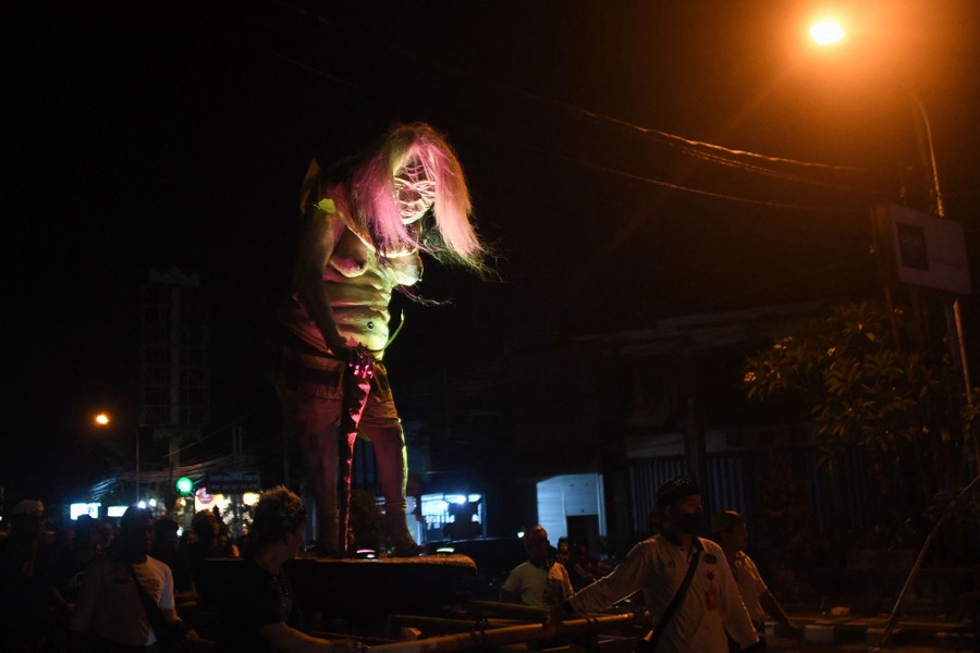 A frightening sculpture resembling a demon with long hair is seen in a nighttime parade, lit from below.