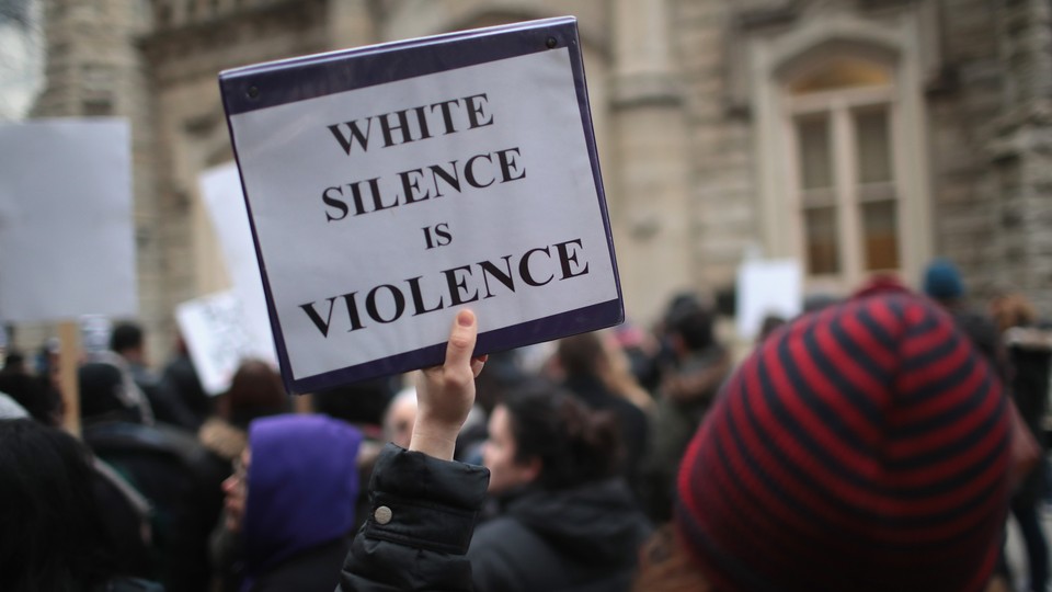 A demonstrator holds a sign saying "White Silence Is Violence"