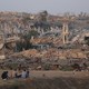 Photograph of destroyed buildings in Gaza with people sitting on the roadside staring at the wreckage