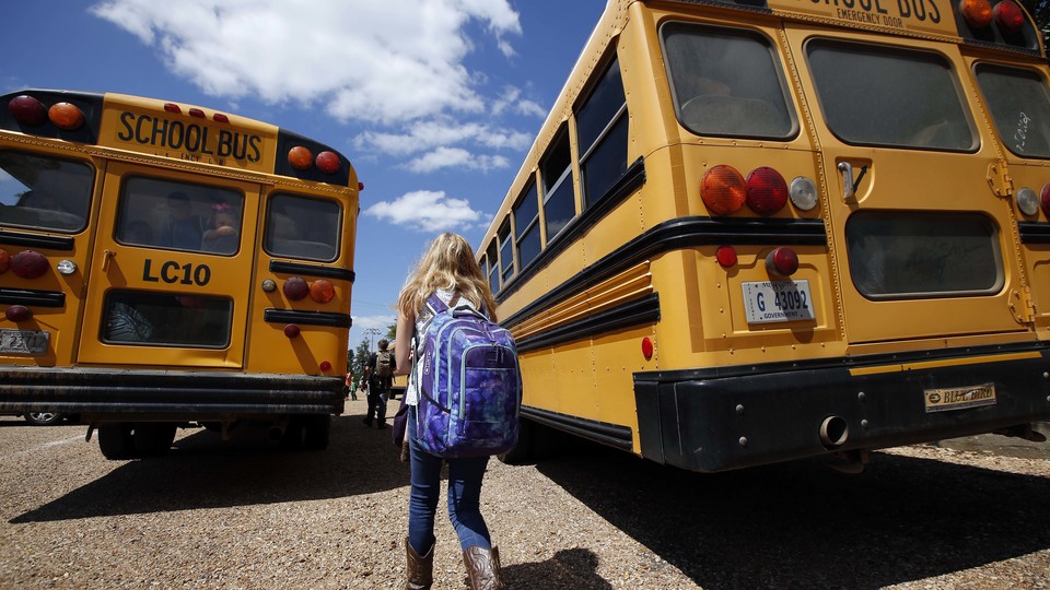 A girl walks toward two school buses.