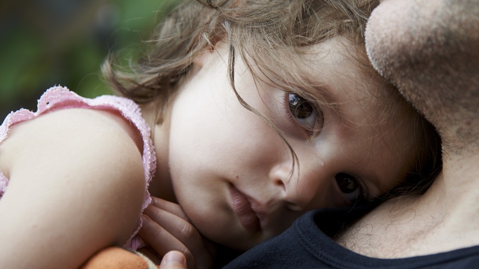 A tear streaks across sad child's nose as she rests her head on a man's chest.