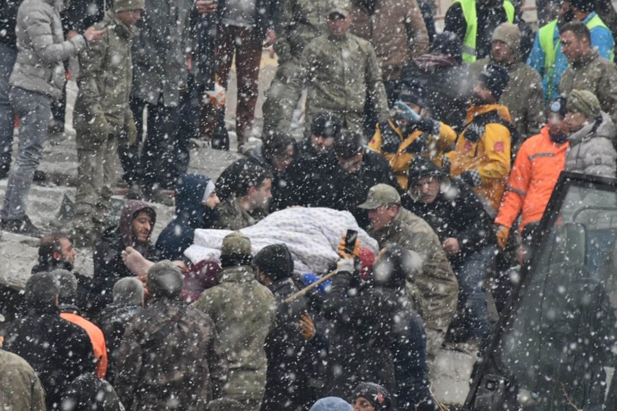 Rescue workers and volunteers carry an injured person away from a damaged building.