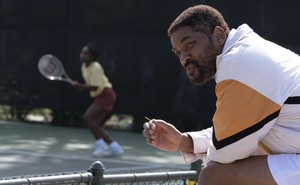 Will Smith sitting by a tennis court where his character's daughter is practicing in "King Richard"