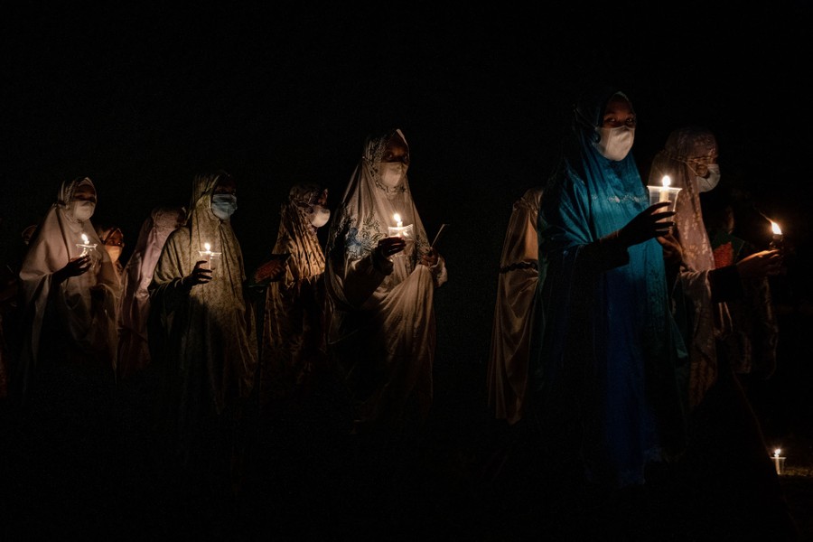 Several young people walk in the dark while carrying candles.