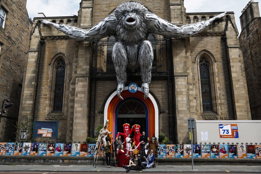 A group of performers stands in front of a venue, beneath a large inflatable gibbon.