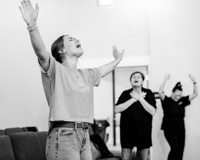 black-and-white photo of woman with arms up, eyes closed, and head back crying out, with other worshippers in background
