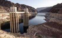 A view of a partially empty reservoir and dam structures, surrounded by rocky hills and cliffs.