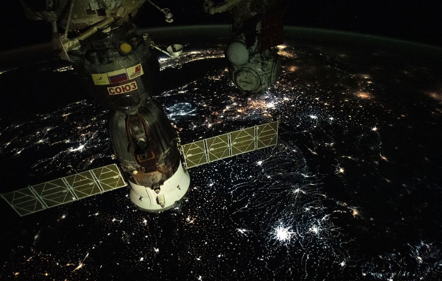A night view of the Soyuz module docked with the ISS as it passes above Eastern Europe, showing many different-colored city lights