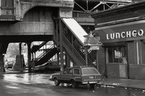 black-and-white photo of Boston's Washington Street Elevated in the 1980s with Dover station exit, diner with "Luncheon" neon sign, wood-paneled station wagon