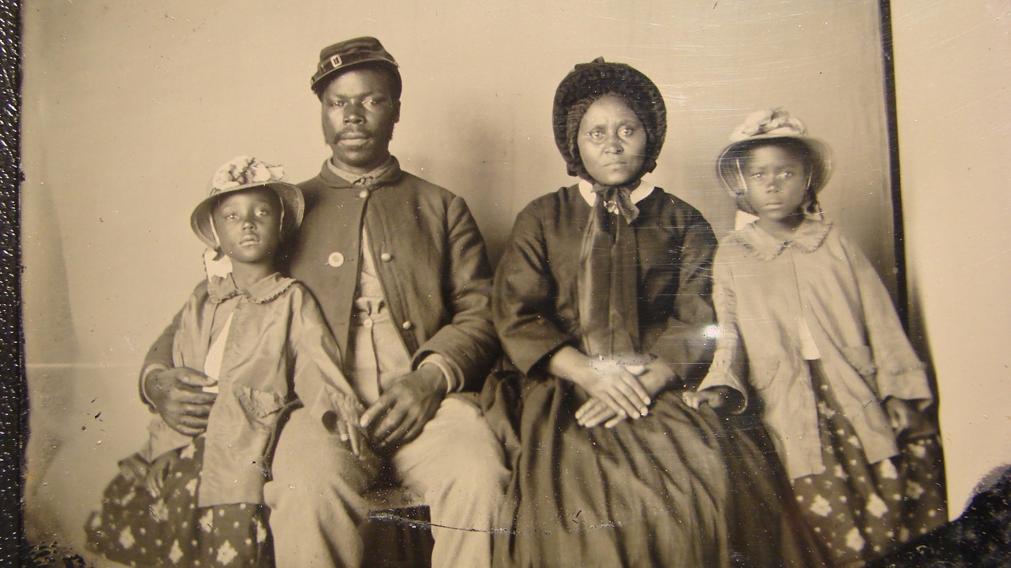 A Black Civil War soldier and his family sit for a portrait in formal clothes.