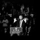Black-and-white picture of Donald Trump speaking to a crowd from a podium with a sign that reads "USA THANK YOU TOUR 2016"