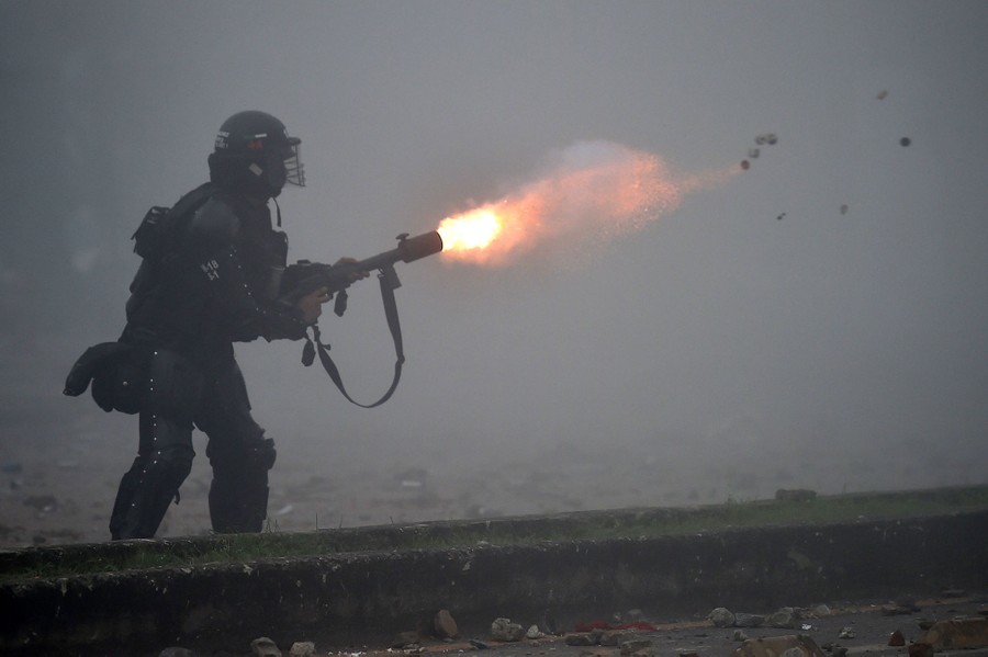A riot police officer fires tear gas.