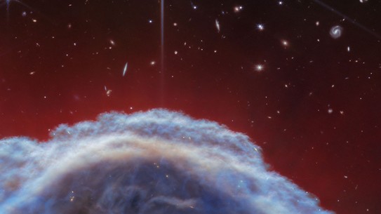 A space telescope image showing part of a cloud-like nebula with stars and galaxies visible in the background
