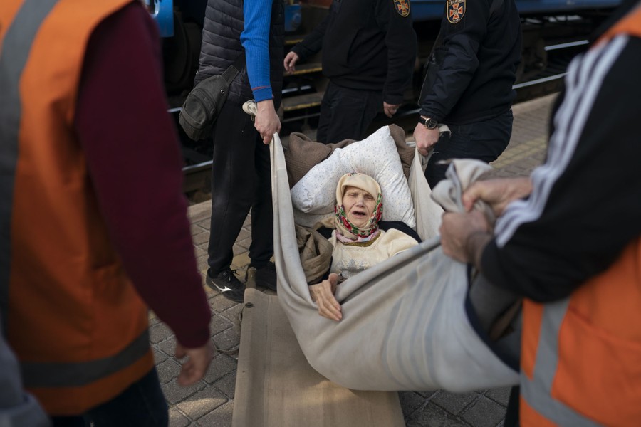Several people use a blanket as a stretcher to lift an elderly woman at a train station.