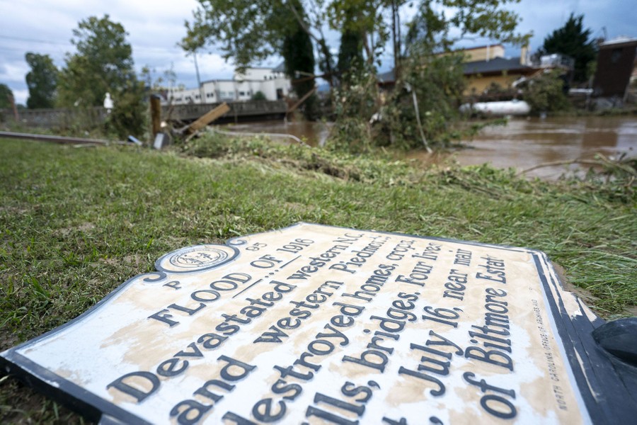 A historic marker sign noting the flood of 1916 lies on the ground next to a flooded waterway.