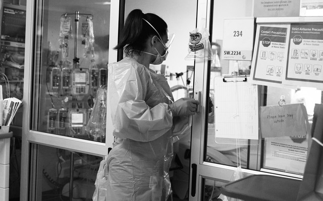 A health-care worker stands in the doorway of a patient's room.