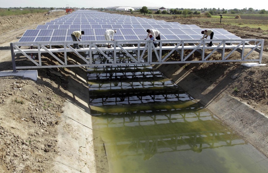 Workers give finishing touches to solar panels installed above a canal.