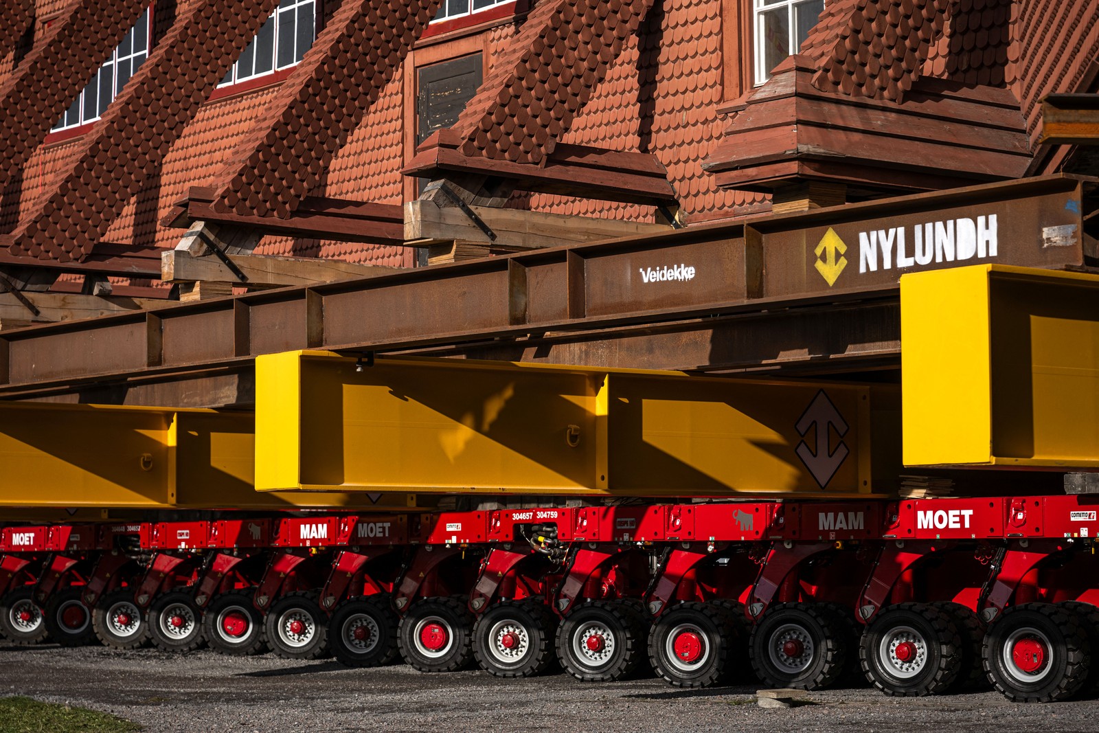 Many-wheeled tractors support immense steel beams that hold up a wooden church.