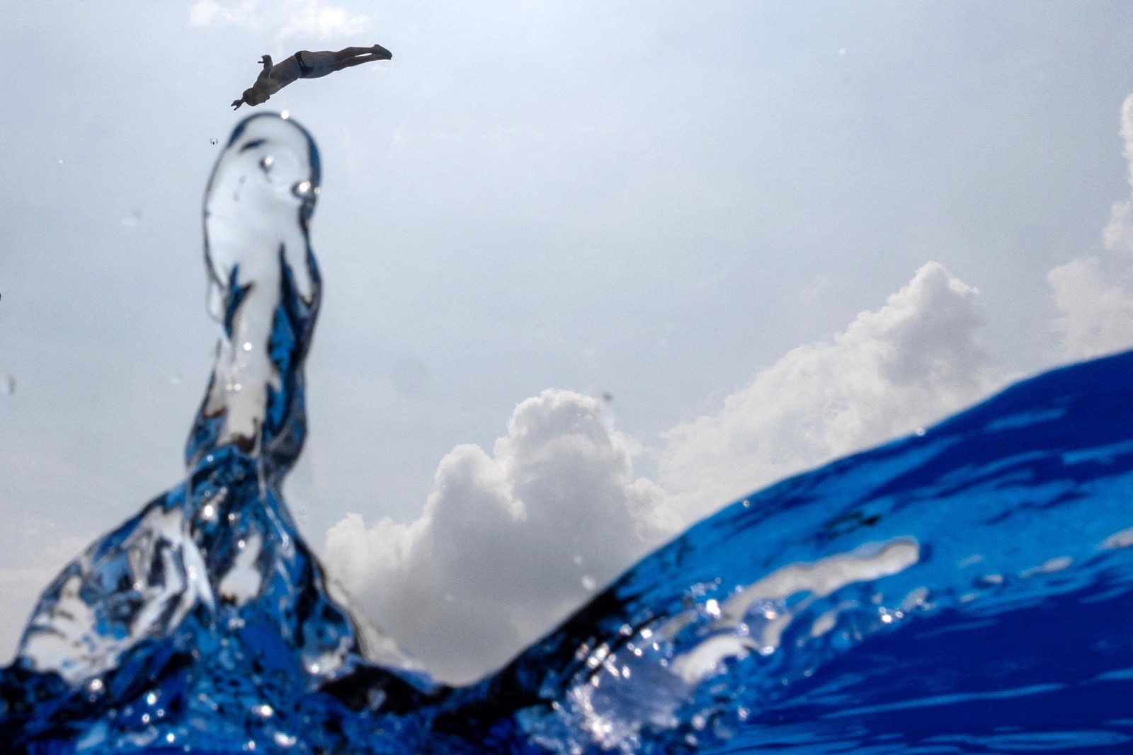 A view of a high diver falling toward the water, seen from the water's surface, with water splashing upward.