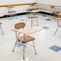 A photo of single-seat desks spaced out in a classroom with white walls and a blue-and-white-tiled floor