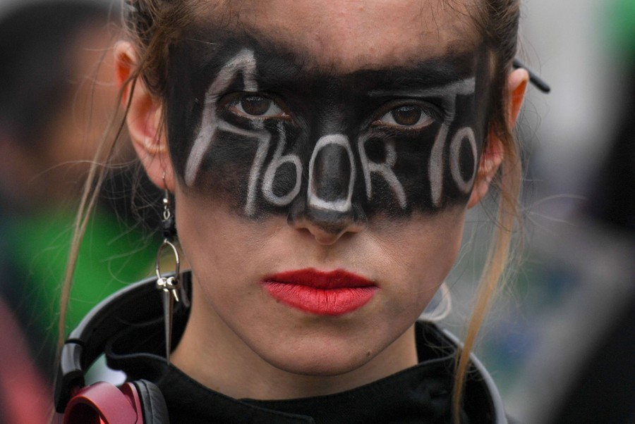 A protester marches with her face painted black around her eyes, and the word "Aborto" written on her face.
