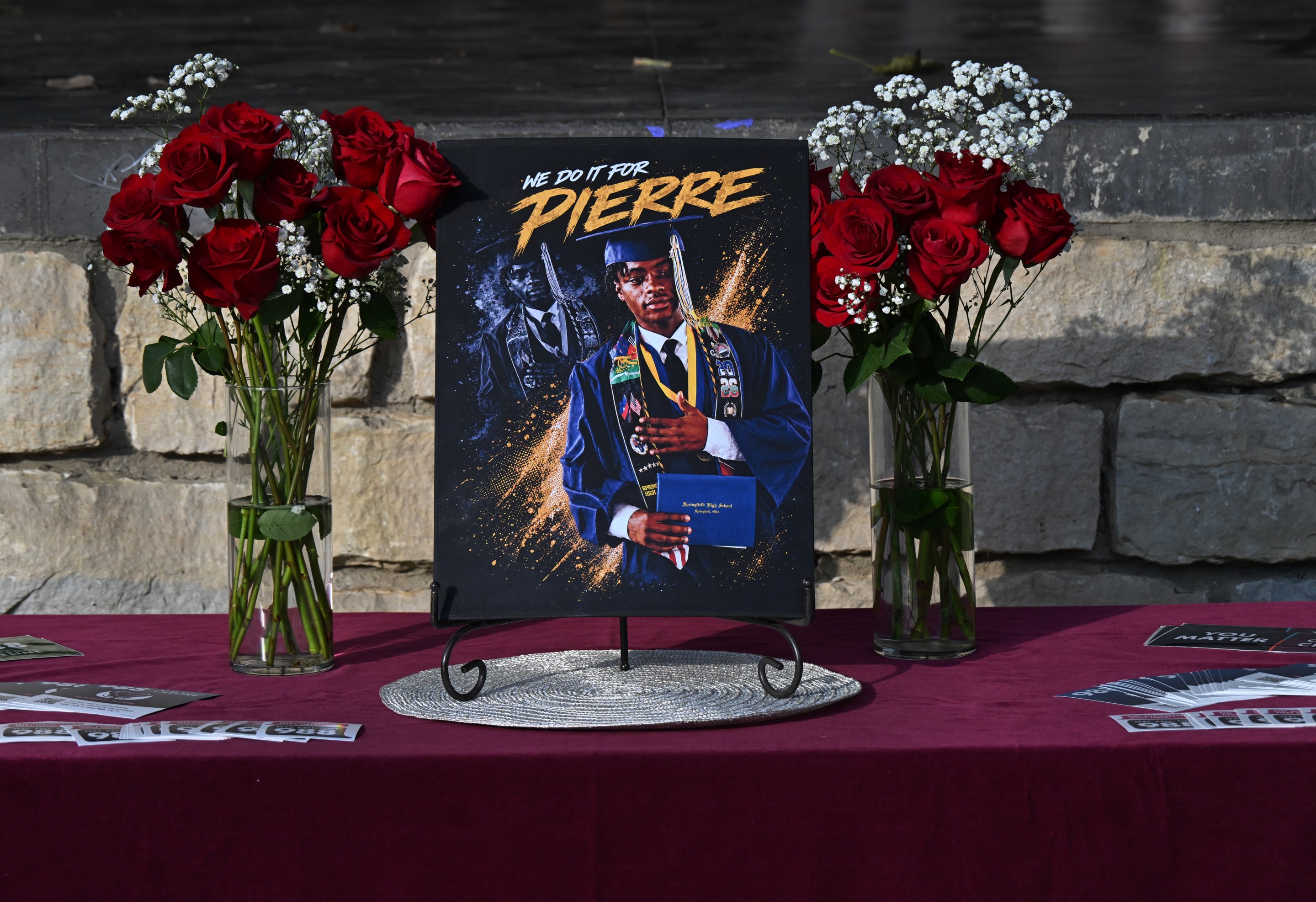 a painting of a boy graduating sits on a table between two vases of roses