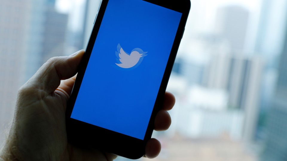A hand hold a phone with the twitter logo on the screen in blue and white.