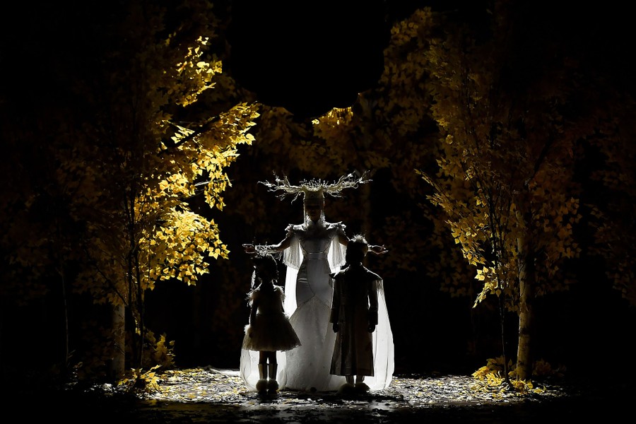 A woman and two children stand silhouetted on a runway during a fashion show.