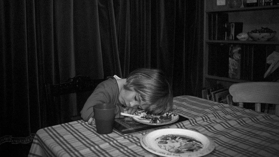 A black-and-white photo of a young girl asleep at the dinner table