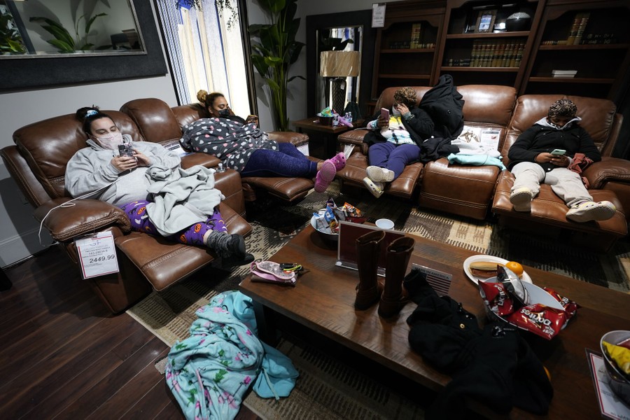 Four people in warm and comfortable clothes rest in floor display recliners in a furniture store.