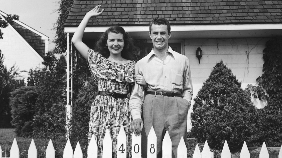 Two people waving over a white picket fence