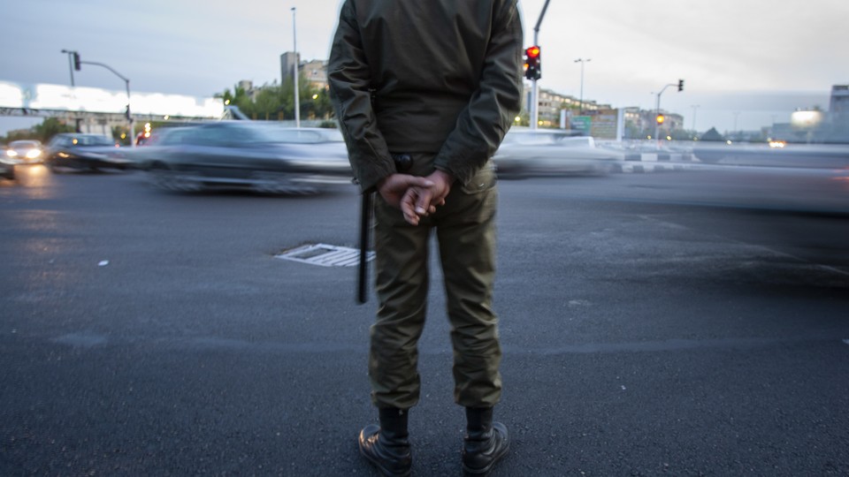 An Iranian police officer stands at a busy traffic intersection.