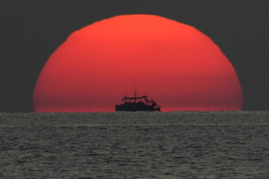 A fishing boat passes in front of the setting sun.
