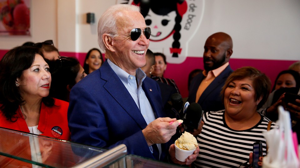 Joe Biden, in sunglasses, smiling with a spoonful of ice cream while surrounded by smiling supporters.