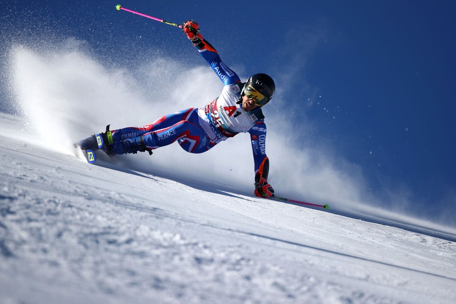A skier races down a snowy hillside, kicking up snow.