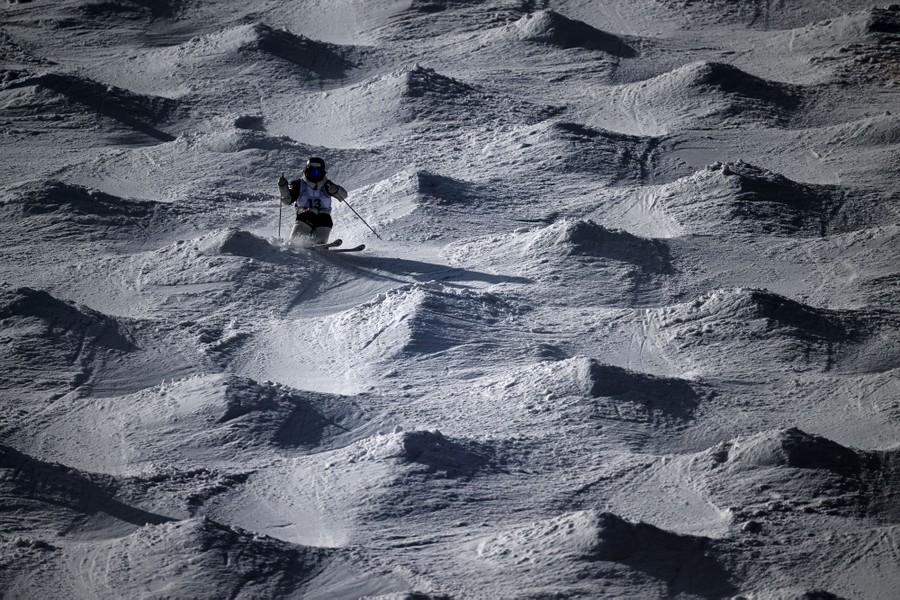 A skier races down a hill covered in moguls.