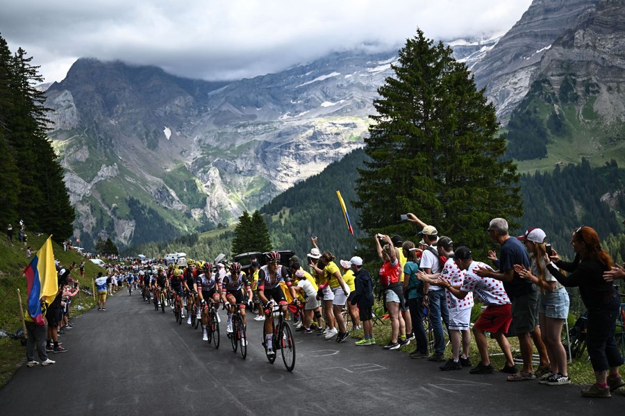 Fans line a mountain road, cheering as cyclists ride past.