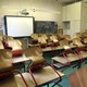 An empty classroom. All the chairs are on top of the desks. There is a Smartboard at the front of the room.