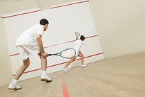 Two people wearing all-white playing squash together