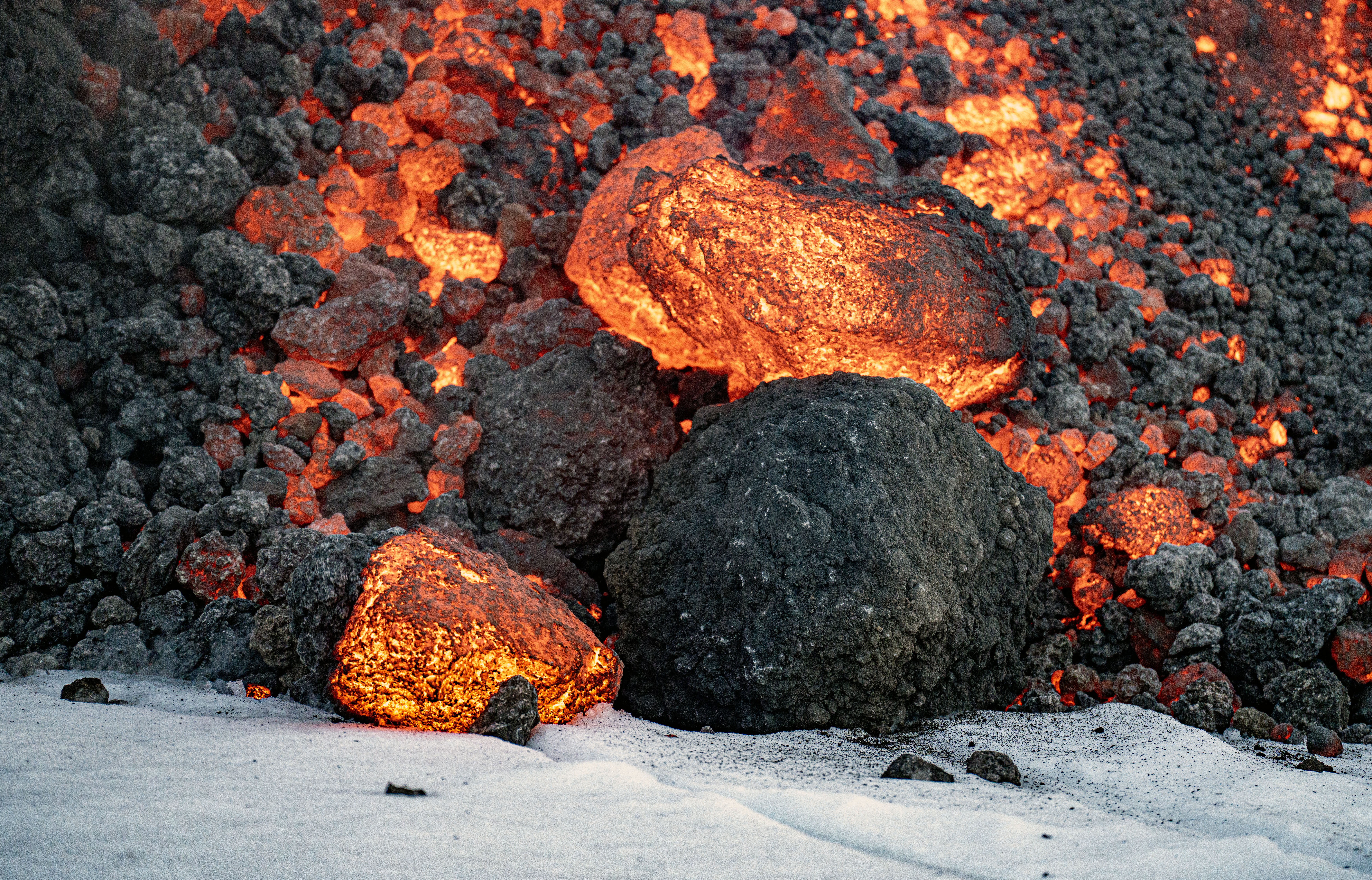 Glowing chunks of lava tumble onto a snow-covered slope.