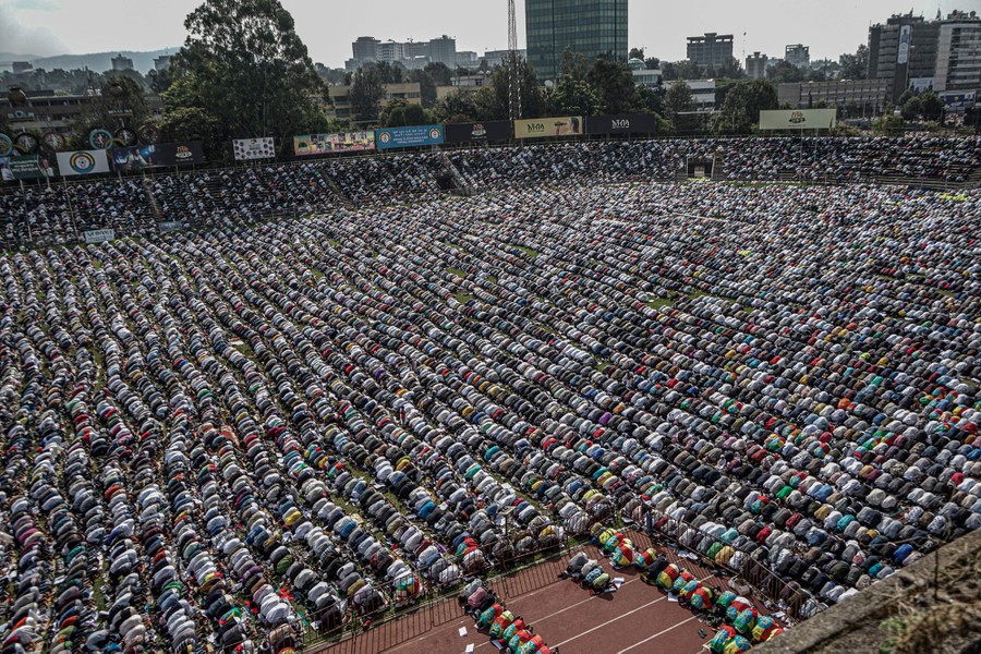 A large group of worshippers gather in a stadium to pray.