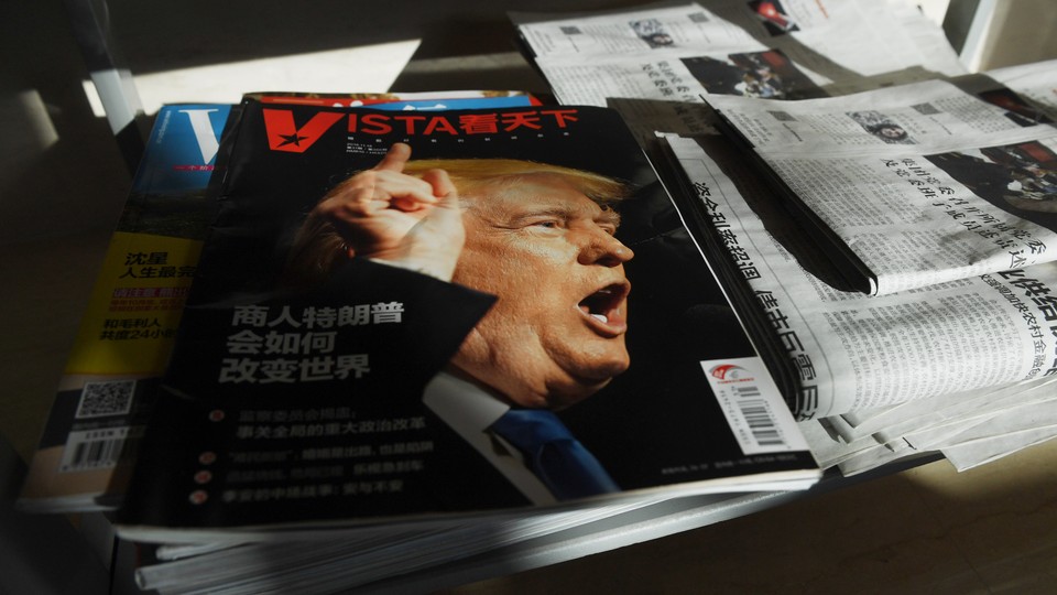 A magazine with a picture of President Donald Trump sits on top of other magazines and newspapers.