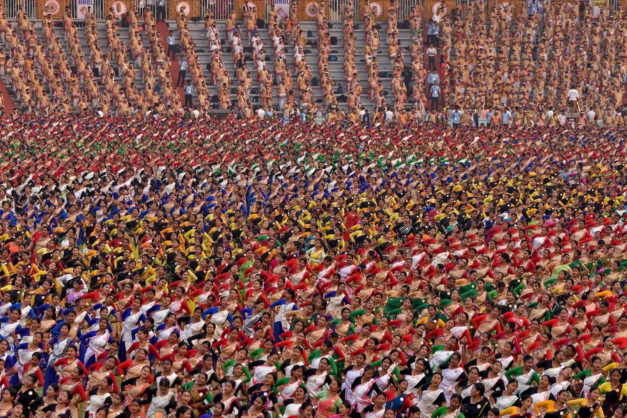 A crowd of thousands performs a traditional dance inside a stadium.