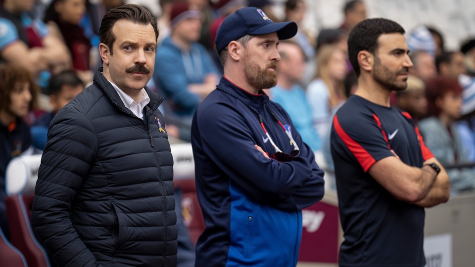 A landscape photo of Ted Lasso, Coach Beard, and Roy Kent from the TV show "Ted Lasso"