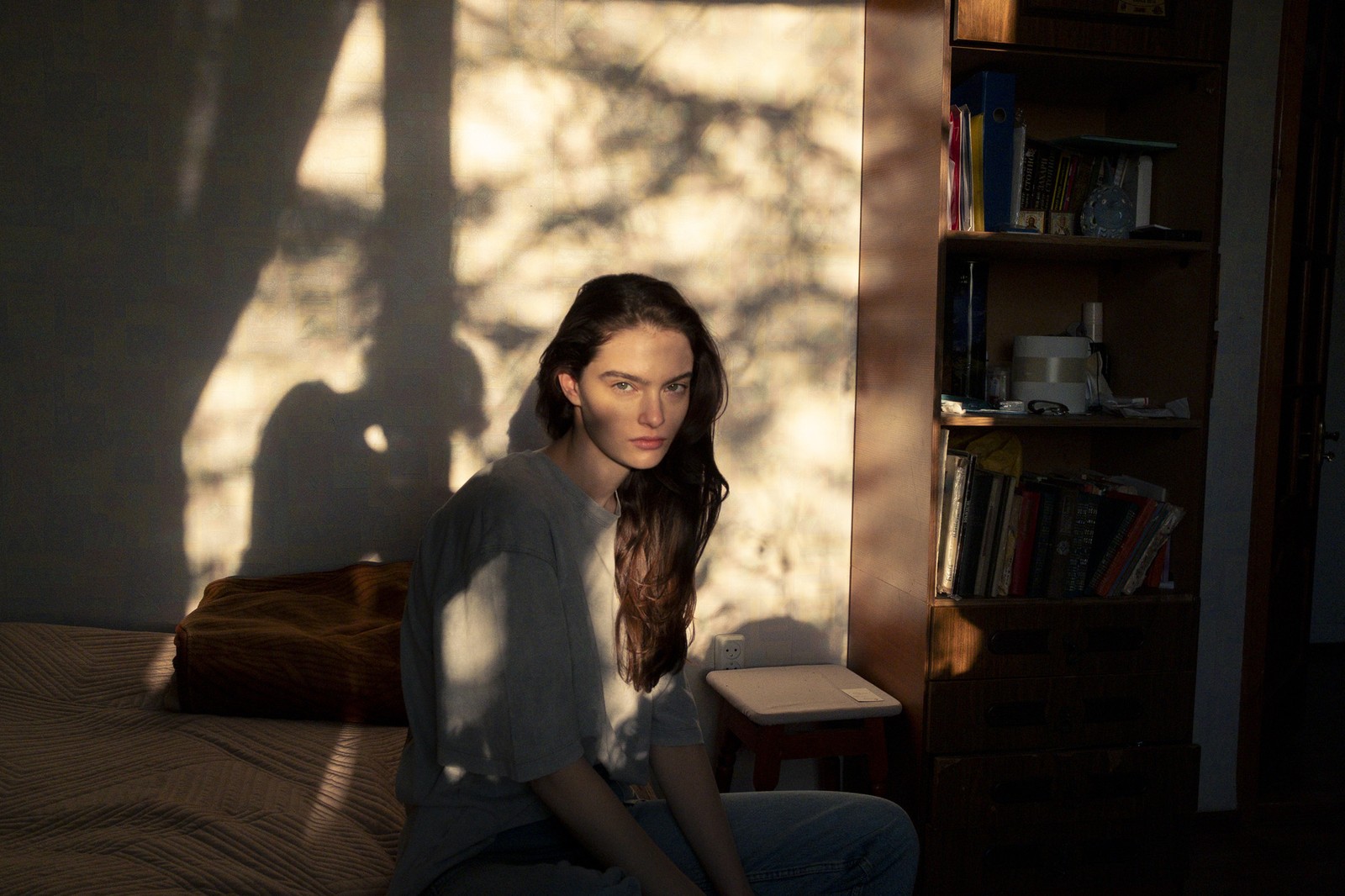 A young woman, seated on a bed in a bedroom