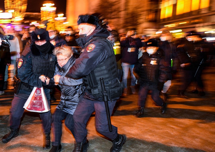 A person is forcibly moved by two police officers, as others watch nearby.